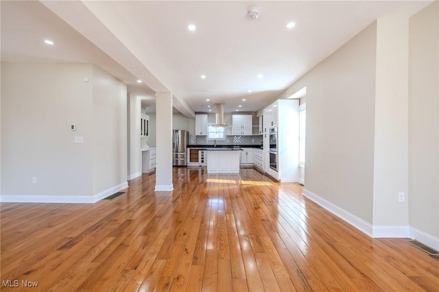 unfurnished living room with light wood finished floors, visible vents, baseboards, recessed lighting, and a sink