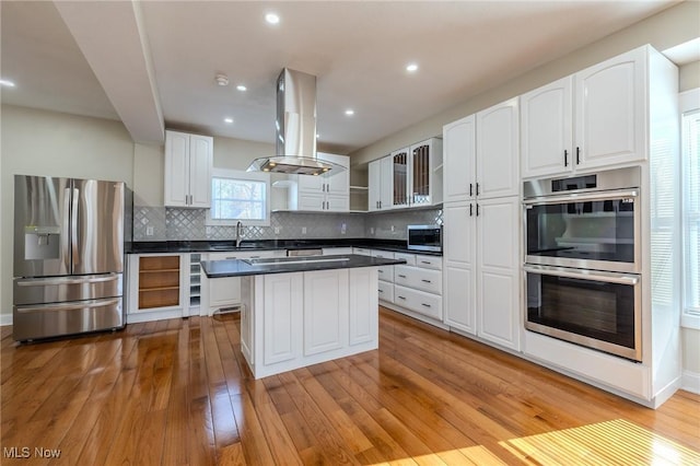 kitchen with light wood-style flooring, island exhaust hood, open shelves, dark countertops, and stainless steel appliances