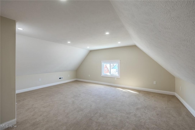 additional living space with visible vents, baseboards, carpet, lofted ceiling, and a textured ceiling