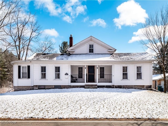 snow covered back of property featuring covered porch and a chimney