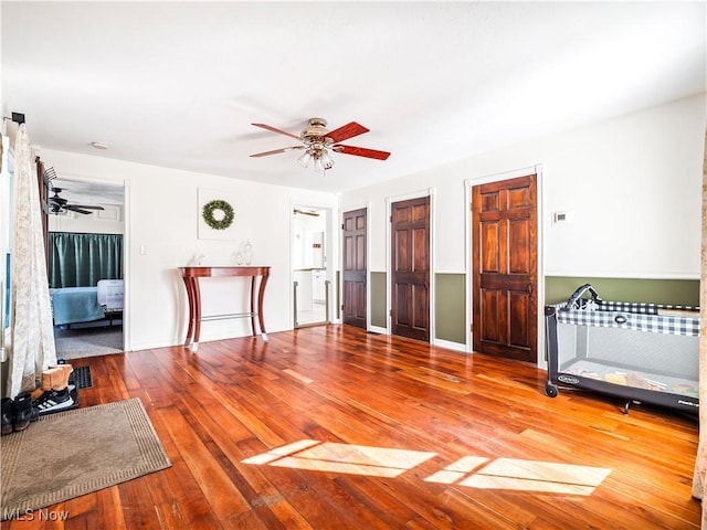 living area with baseboards, wood-type flooring, and a ceiling fan