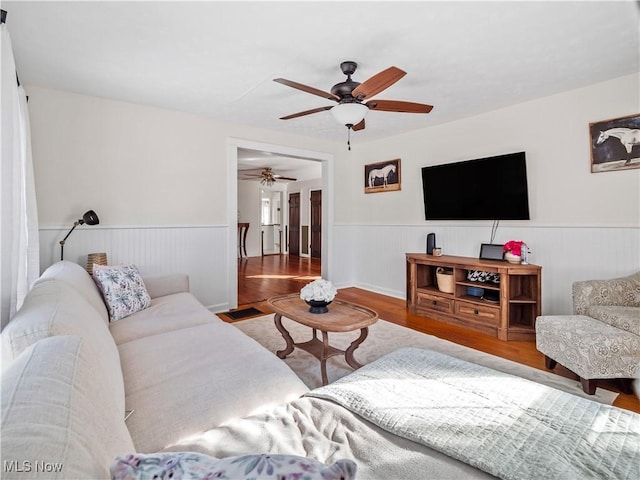 living area with wood finished floors, a ceiling fan, and wainscoting