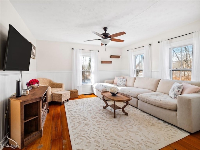 living area with a wainscoted wall, ceiling fan, and dark wood-style flooring