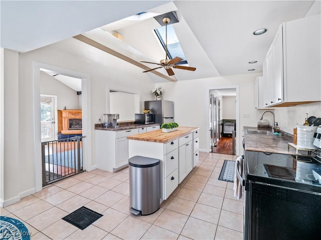 kitchen with light tile patterned floors, vaulted ceiling with skylight, appliances with stainless steel finishes, wood counters, and a sink