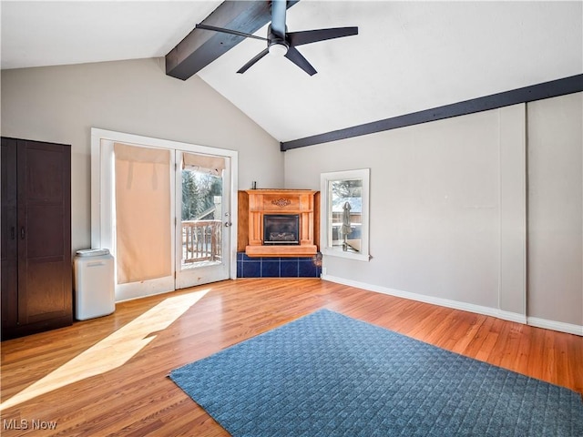 unfurnished living room featuring a tiled fireplace, lofted ceiling with beams, a ceiling fan, and wood finished floors