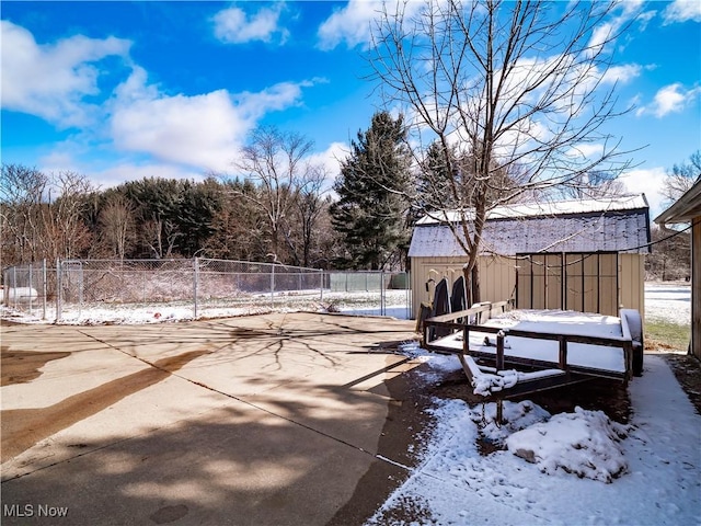 yard covered in snow featuring a storage shed, fence, an outbuilding, and a patio area