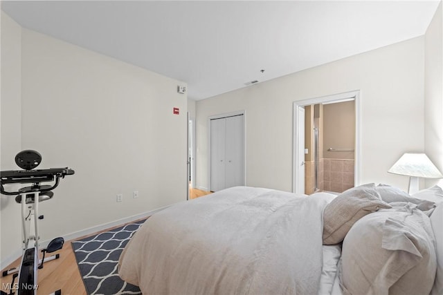 bedroom with visible vents, connected bathroom, baseboards, wood finished floors, and a closet