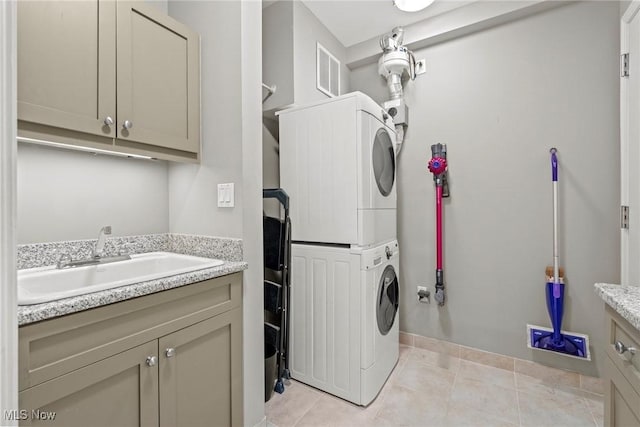 laundry area featuring visible vents, stacked washer and clothes dryer, light tile patterned flooring, cabinet space, and a sink