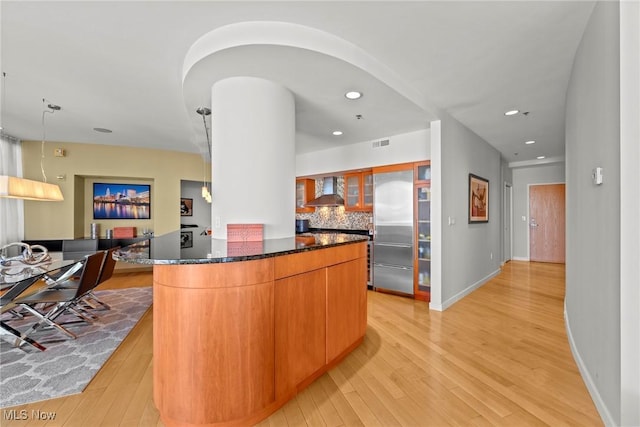 kitchen with glass insert cabinets, tasteful backsplash, light wood-style floors, and wall chimney range hood