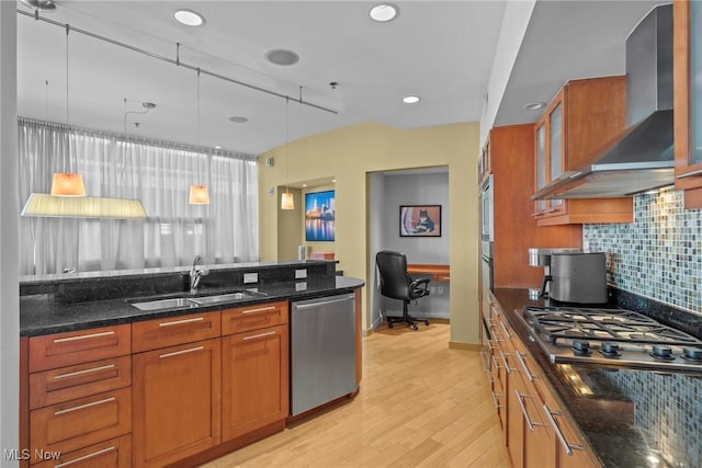 kitchen featuring tasteful backsplash, wall chimney range hood, brown cabinetry, stainless steel appliances, and a sink