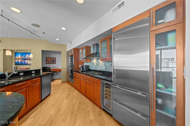 kitchen featuring visible vents, wall chimney range hood, beverage cooler, built in appliances, and a sink