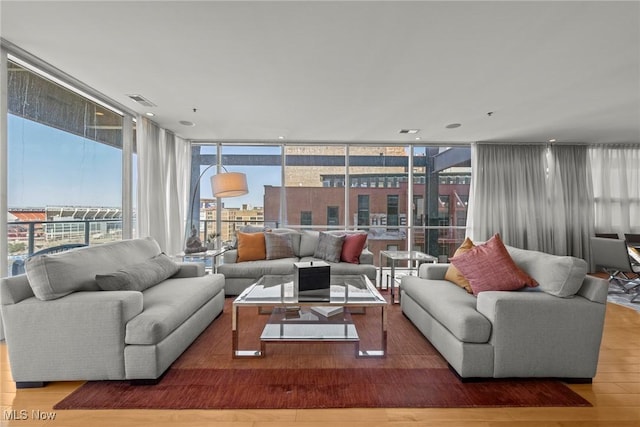 living area with a healthy amount of sunlight, wood finished floors, visible vents, and expansive windows