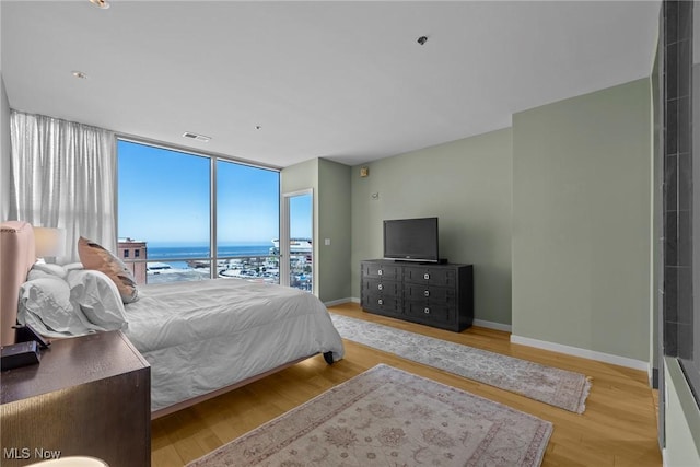 bedroom with visible vents, a wall of windows, baseboards, and wood finished floors