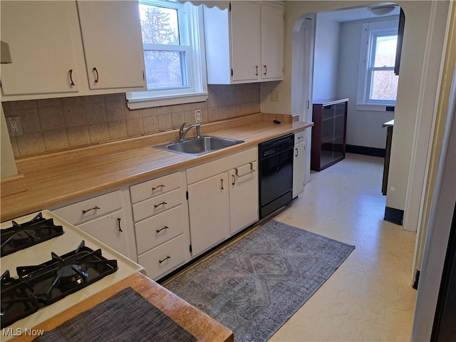 kitchen featuring dishwasher, light countertops, arched walkways, white cabinets, and a sink