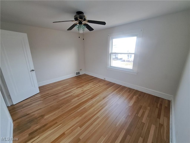 spare room with light wood finished floors, visible vents, a ceiling fan, and baseboards