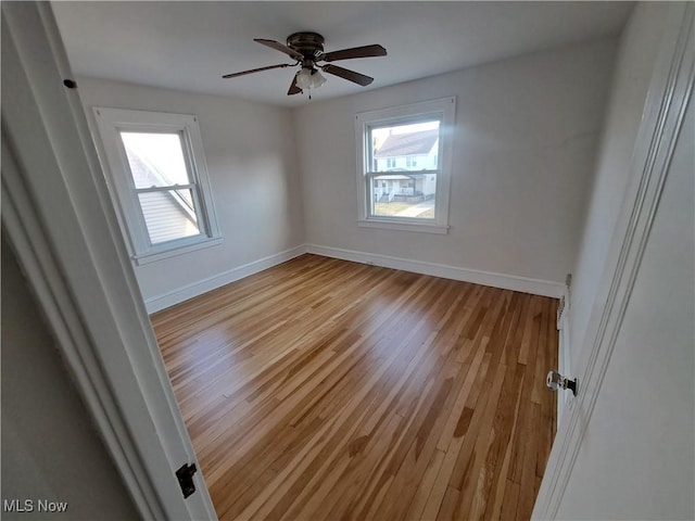 unfurnished room with light wood-style flooring, a ceiling fan, and baseboards