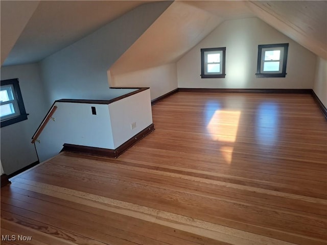 additional living space with baseboards, light wood-style floors, and vaulted ceiling