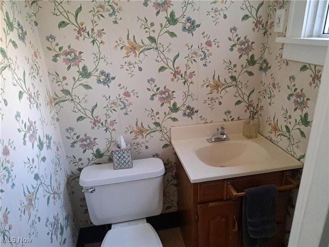 half bathroom featuring toilet, vanity, and wallpapered walls