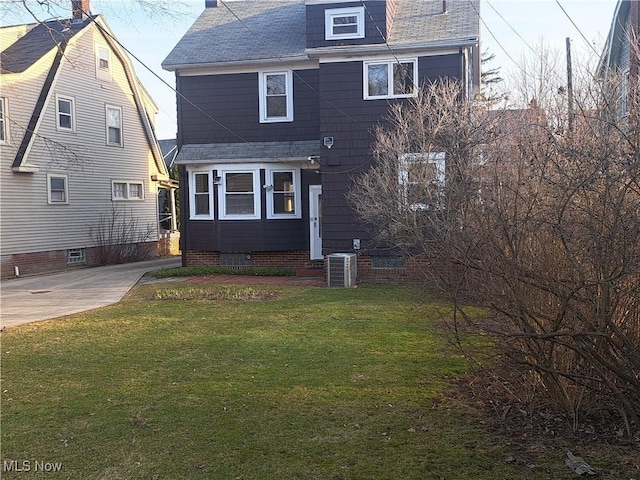 back of house featuring crawl space, cooling unit, a shingled roof, and a yard