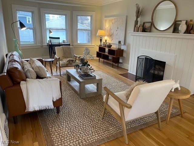 living area featuring crown molding, a fireplace with flush hearth, and wood finished floors