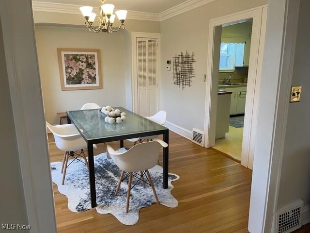 dining room with a chandelier, visible vents, crown molding, and wood finished floors