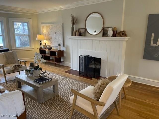 living area featuring a fireplace with flush hearth, wood finished floors, baseboards, and ornamental molding