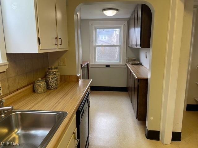 kitchen featuring baseboards, arched walkways, a sink, decorative backsplash, and white cabinetry