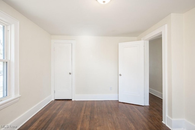 spare room featuring a healthy amount of sunlight, baseboards, and dark wood-style flooring