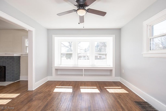 empty room with hardwood / wood-style flooring, a brick fireplace, baseboards, and visible vents