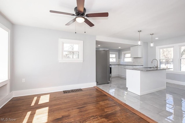 kitchen featuring a ceiling fan, baseboards, freestanding refrigerator, a sink, and tasteful backsplash