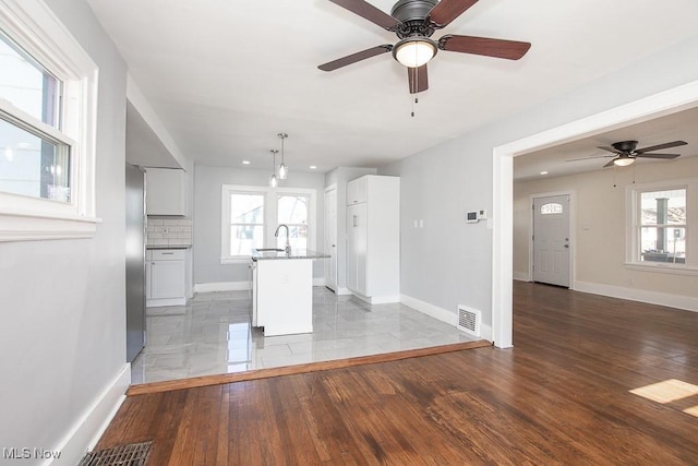 unfurnished living room featuring visible vents, a sink, light wood finished floors, baseboards, and ceiling fan