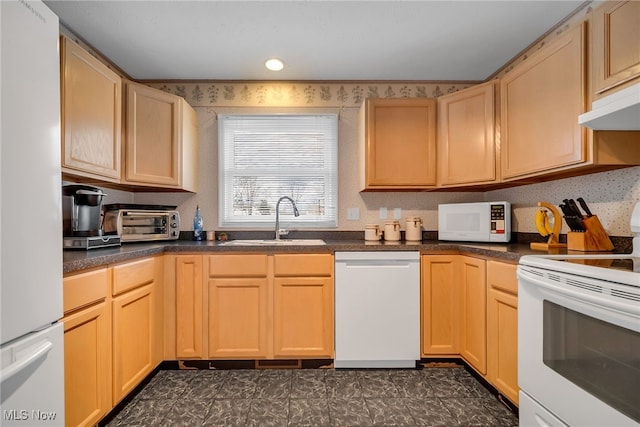 kitchen with white appliances, wallpapered walls, a sink, under cabinet range hood, and dark countertops