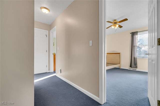 corridor with dark colored carpet, visible vents, and baseboards