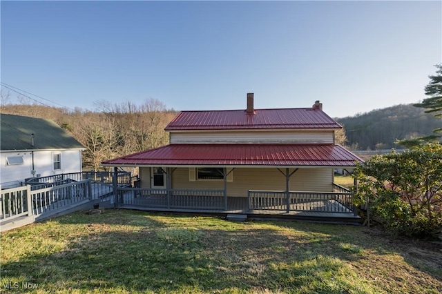 rear view of property featuring a chimney, covered porch, metal roof, and a yard