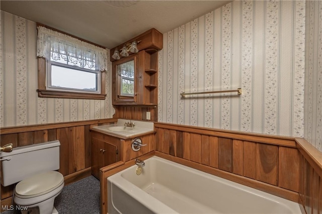 full bath featuring a garden tub, toilet, wainscoting, wallpapered walls, and vanity