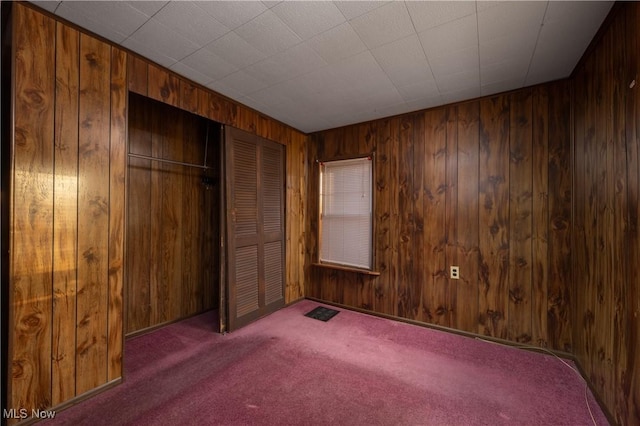 unfurnished bedroom featuring wooden walls, a closet, and carpet floors