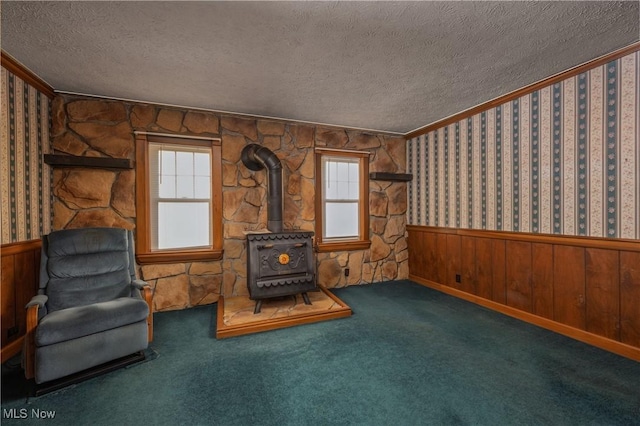 unfurnished room with carpet, a wainscoted wall, wallpapered walls, a wood stove, and a textured ceiling