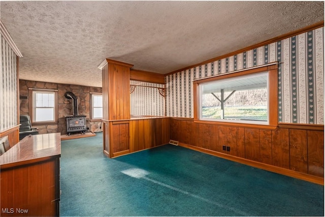 kitchen featuring a wainscoted wall, a textured ceiling, wallpapered walls, and a wood stove