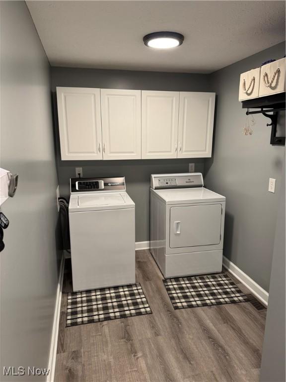 clothes washing area with cabinet space, wood finished floors, baseboards, and separate washer and dryer