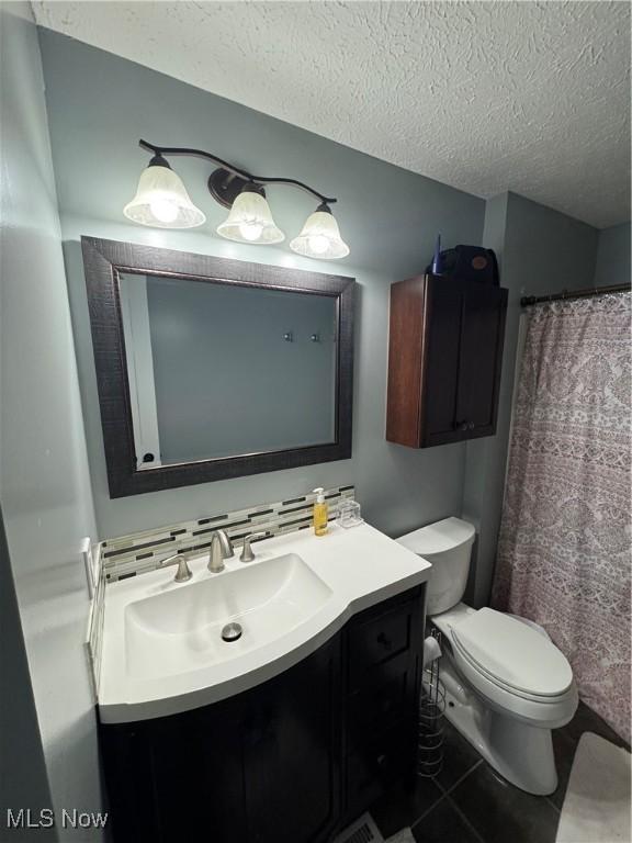 bathroom featuring tile patterned flooring, backsplash, toilet, vanity, and a textured ceiling