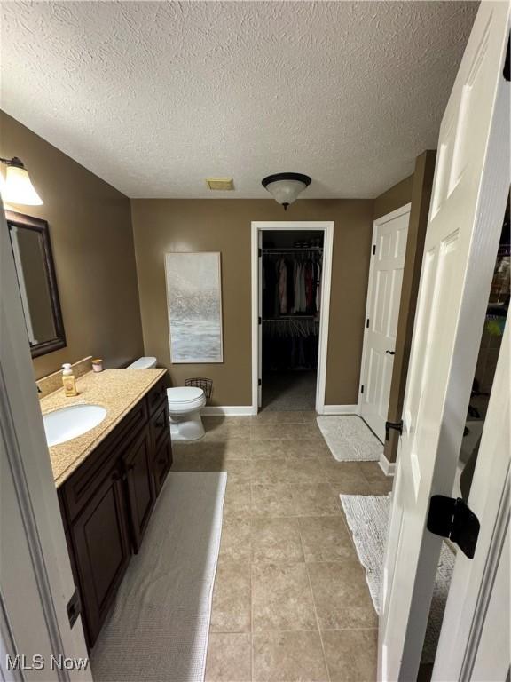 bathroom featuring vanity, baseboards, visible vents, a walk in closet, and toilet