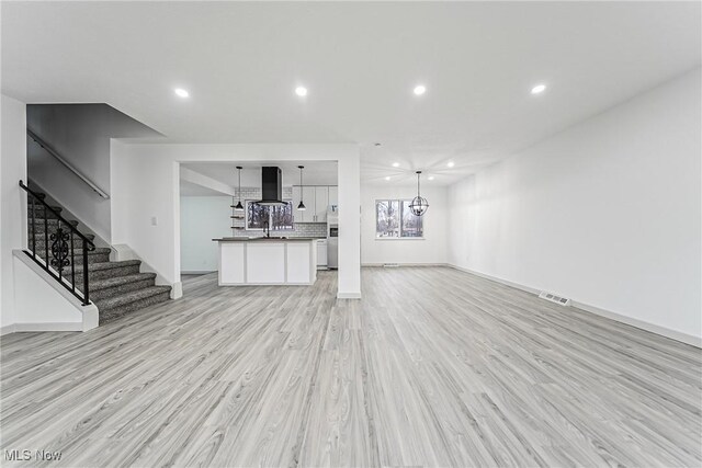 unfurnished living room with light wood-type flooring, a sink, recessed lighting, stairway, and a chandelier