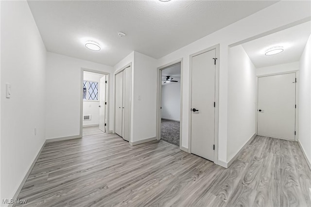 corridor with visible vents, baseboards, and light wood finished floors