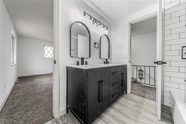 bathroom with double vanity, wood finished floors, a tub to relax in, and a sink