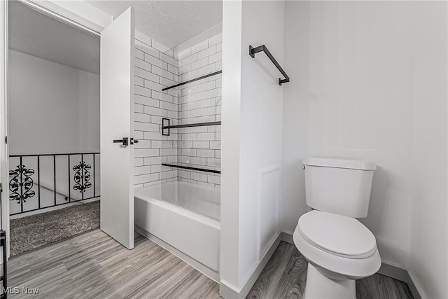 bathroom featuring a textured ceiling, wood finished floors, baseboards, shower / bath combination, and toilet