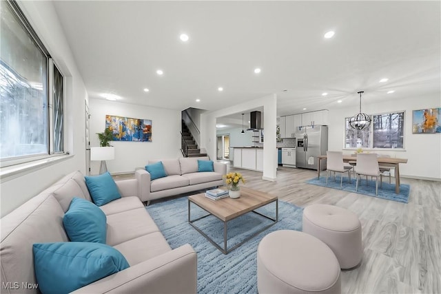 living area with recessed lighting, light wood-type flooring, stairs, and an inviting chandelier