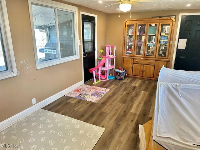 recreation room featuring ceiling fan, baseboards, a textured ceiling, and wood finished floors