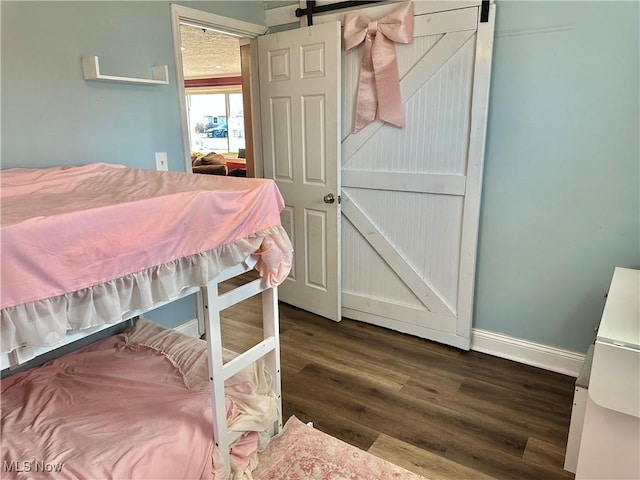 bedroom featuring a barn door, baseboards, and dark wood-style flooring