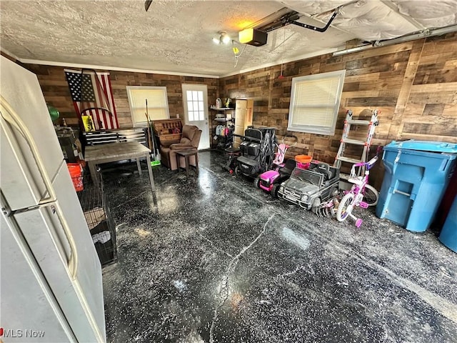 garage with wooden walls, a garage door opener, and freestanding refrigerator