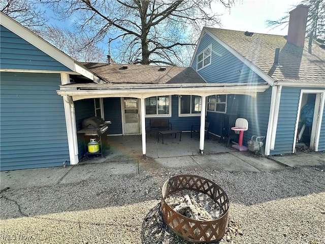 rear view of property featuring a chimney, a patio, and a shingled roof